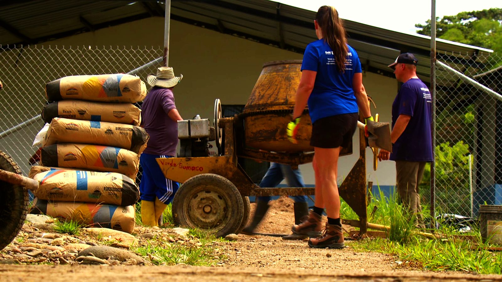 Guild volunteers working the cement mixer beside a stack of cement bags